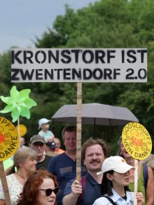 Kronstorf ist Zwentendorf 2.0, ein Demoschild, das von einem Aktivisten in die Luft gehalten wird. Rings herum sind weitere protestierende Menschen. Man sieht ein weiteres Schild mit Googlhupf? Nein Danke, im Stil der Antiatom Sticker.